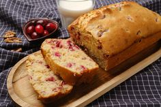 a loaf of cranberry bread sitting on top of a wooden cutting board next to a glass of milk