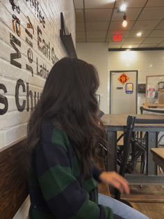 a woman sitting on top of a wooden bench next to a wall covered in writing