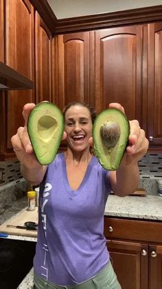 a woman holding an avocado up to her face in the middle of a kitchen