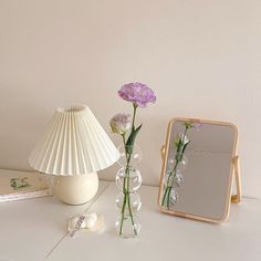 a white table topped with a vase filled with flowers next to a mirror and a tape measure