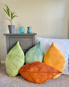 four leaf shaped pillows sitting on the floor next to a dresser and potted plant