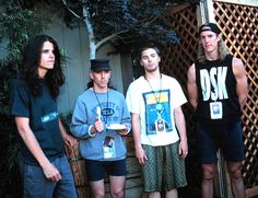 four young men standing next to each other in front of a wooden fence and tree