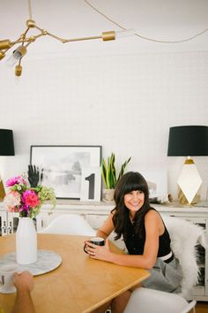 a woman sitting at a wooden table in front of a vase with flowers on it