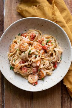 pasta with shrimp and tomato sauce in a white bowl on a wooden table next to a yellow napkin