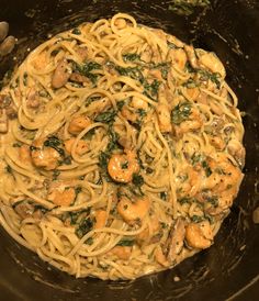 pasta with shrimp and spinach is in a black bowl on the stove top, ready to be cooked