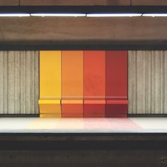 an empty bench in front of a multicolored wall with columns on the other side