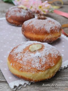 three donuts with powdered sugar on them are sitting on a doily next to flowers