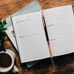 an open book sitting on top of a wooden table next to a cup of coffee