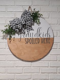 a wooden sign hanging on the side of a white brick wall that says grandkids spoiled here