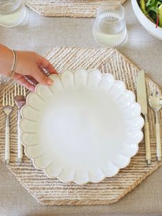 a person holding a white plate on top of a place mat with utensils