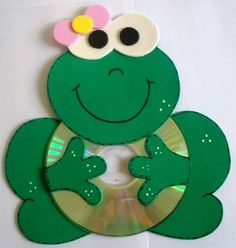 a green frog with a pink flower on its head is sitting in front of a cd