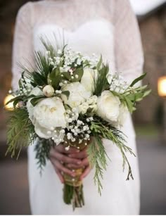 a bride holding a bouquet of white flowers and greenery