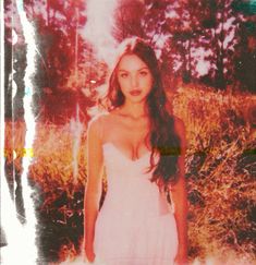 an old photo of a woman in a white dress posing for the camera with trees and grass behind her