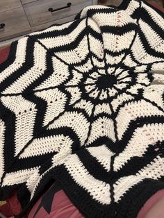 a black and white crocheted blanket on top of a bed next to a dresser