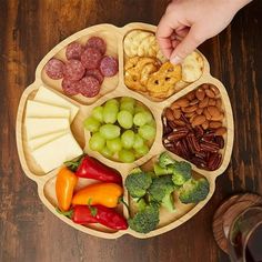 a person is holding their finger over a platter of food that includes grapes, broccoli, crackers and nuts