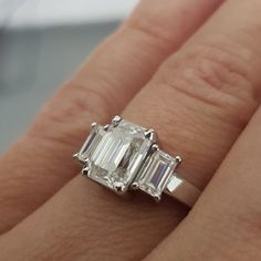 a woman's engagement ring with three baguettes on the side and an emerald cut diamond in the middle