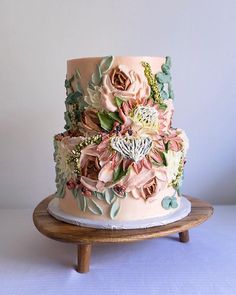 a three tiered cake decorated with flowers and leaves on a wooden stand against a white wall