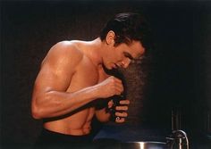 a shirtless man standing in front of a sink