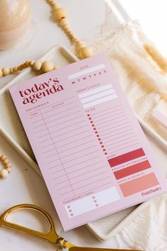 a pink agenda sitting on top of a table next to some gold scissors and beads