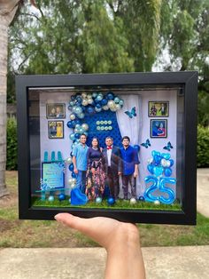 a person holding up a photo frame with balloons and decorations on the wall in front of them