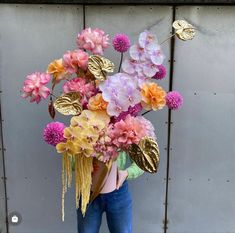 a person holding a bouquet of flowers in front of a gray wall with gold leaves