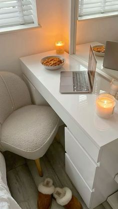 a laptop computer sitting on top of a desk next to a white chair and candle