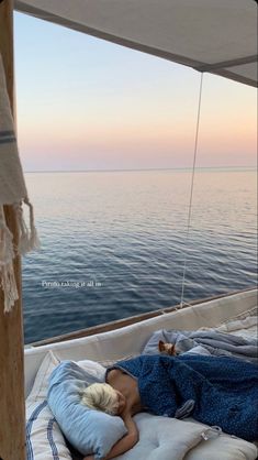 a woman laying on top of a bed under a blanket next to the ocean at sunset