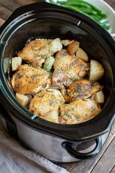 a crock pot filled with chicken and potatoes on top of a wooden table next to green beans