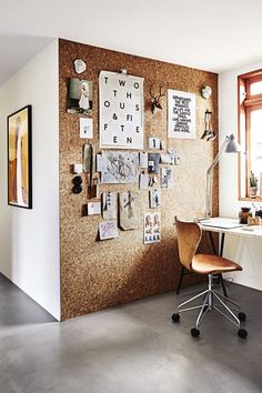 a room with a desk and chair next to a corkboard wall that has pictures on it