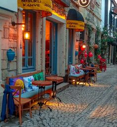 a cobblestone street lined with tables and chairs next to tall buildings at night