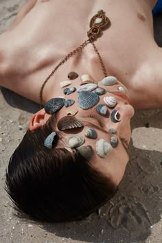 a man laying on the ground with his face covered in sea shells and chains attached to his head