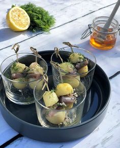 four glasses filled with food sitting on top of a tray next to lemons and parsley