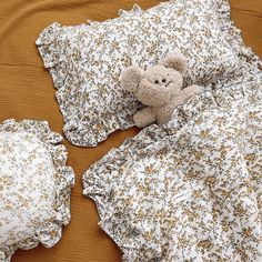 a brown teddy bear laying on top of a bed covered in white and yellow flowers