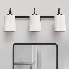 three white lamps are hanging on the wall above a mirror with a reflection in it