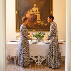 two women standing at a table in front of a painting