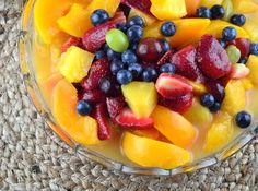 a glass bowl filled with fruit on top of a woven place mat next to a straw bag