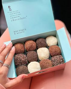 a woman holding a box of chocolates on top of a pink table with other items in it