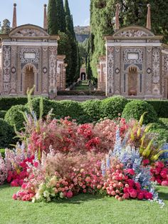 the garden is full of colorful flowers and plants in front of an ornate building with columns