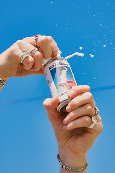 a person holding up a can of beer in the air with bubbles coming out of it