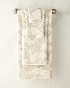 two towels hanging on a towel rack in front of a marble wall with white flowers