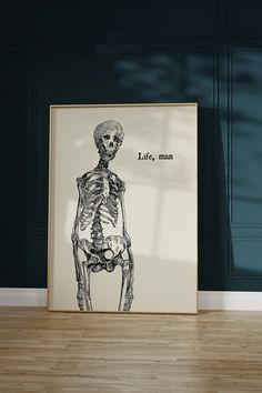 a skeleton sitting on top of a wooden floor in front of a framed poster with the words life man