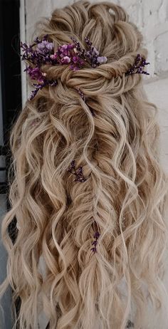 a blonde woman with long curly hair and purple flowers in her hair is shown from the back