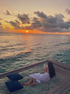 a woman laying in a hammock on the beach at sunset with her back to the camera