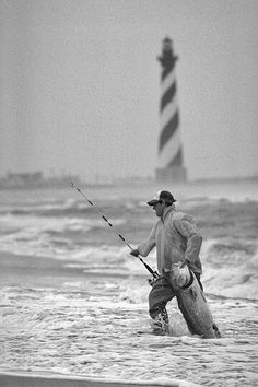 two men fishing in the ocean near a lighthouse