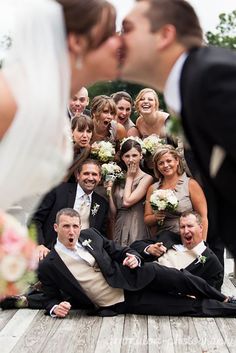 a bride and groom kissing on the ground with their wedding party in the backgroud