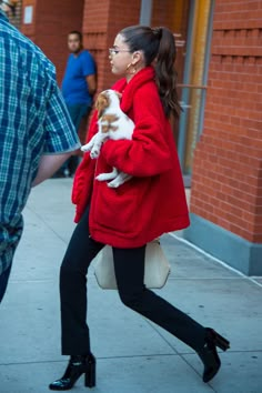 a woman walking down the street with a dog in her lap and wearing a red coat