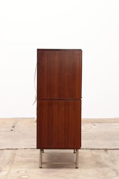 a tall wooden cabinet sitting on top of a cement floor next to a white wall