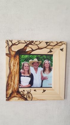 two women and a man are standing in front of a tree with birds on it