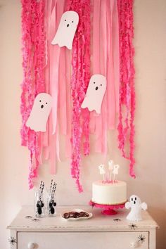 a table topped with a cake covered in icing and pink streamers hanging from the ceiling