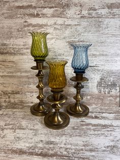 three different colored glass vases sitting next to each other on a white wooden surface